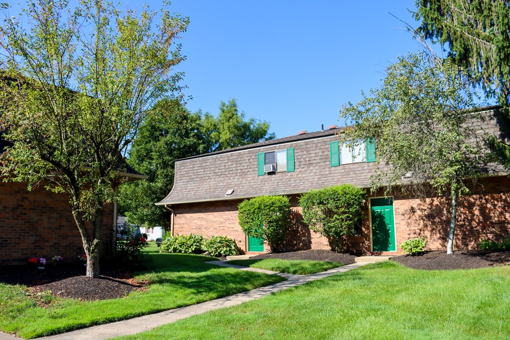 a brick house with green doors and a lawn