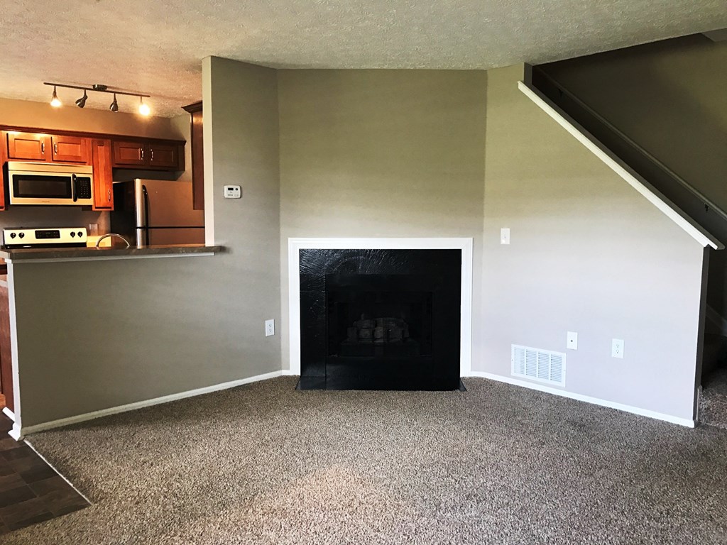 an empty living room with a fireplace and a kitchen