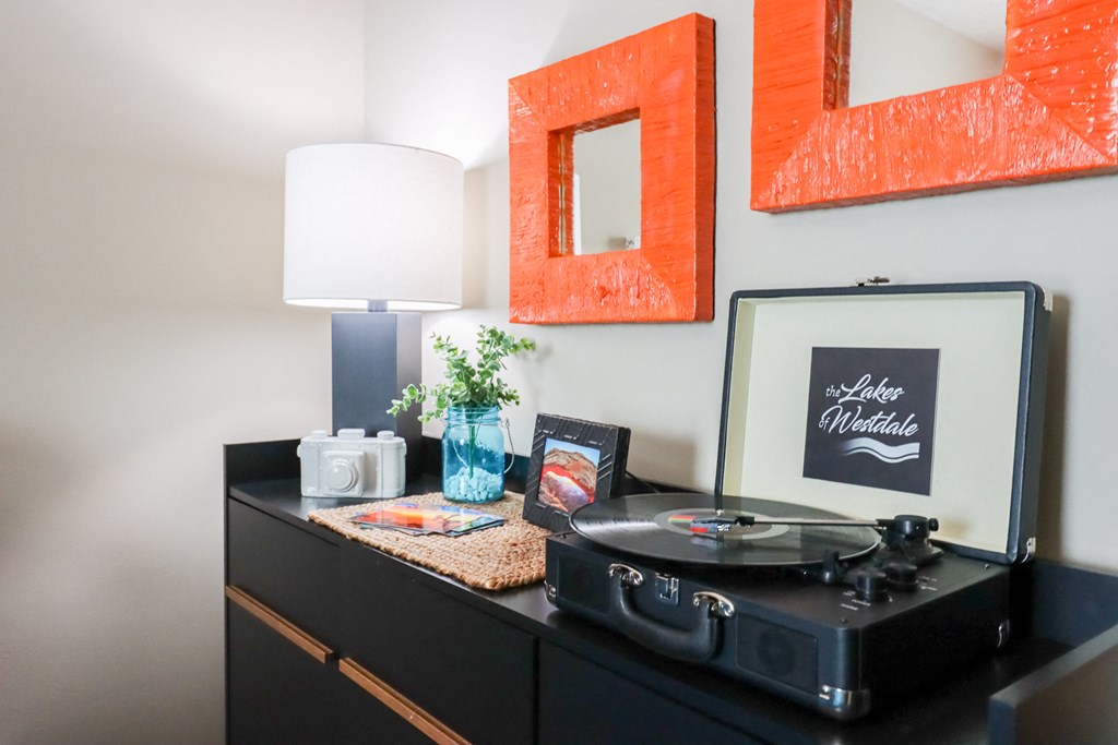 a record player on a dresser in a living room with a lamp and pictures
