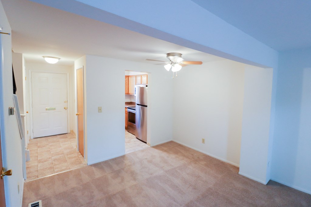 an empty living room with a ceiling fan and a kitchen