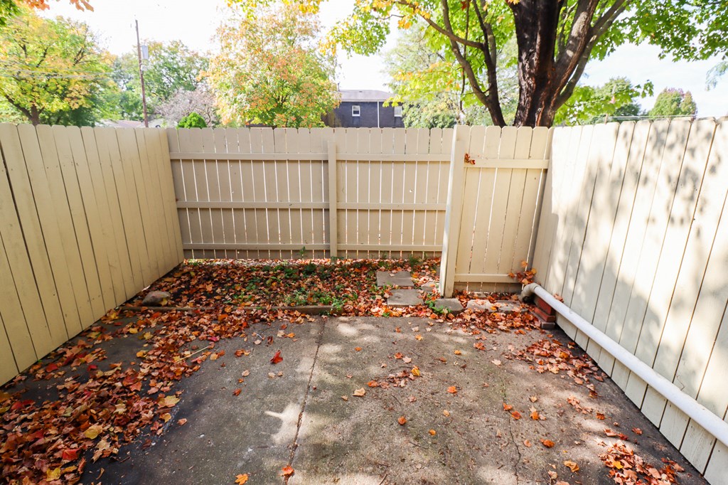 a backyard with a white fence and a tree and leaves on the ground