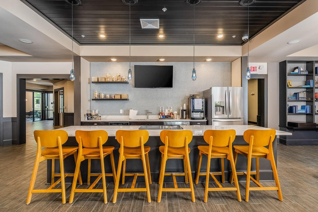 a bar with yellow chairs in front of a kitchen and a television