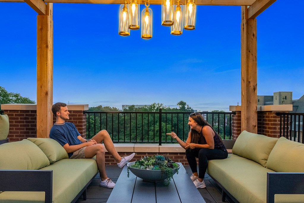 a man and a woman sit on a porch with green couches and a table with a