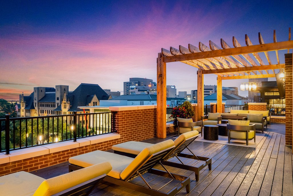 a rooftop deck with lounge chairs and a pergola at sunset