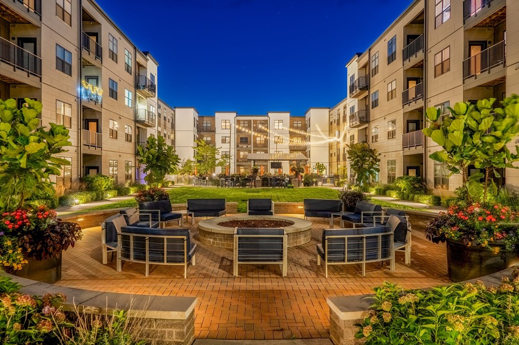 an outdoor area with a fire pit and chairs in front of an apartment building