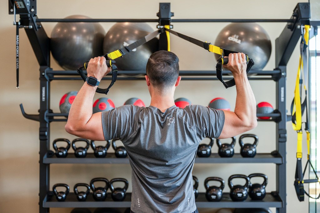 A man is exercising with a TRX suspension trainer in a gym.
