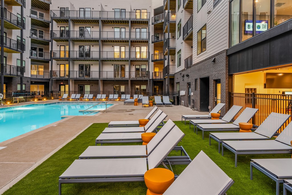 A pool area with sun loungers and apartment buildings in the background.