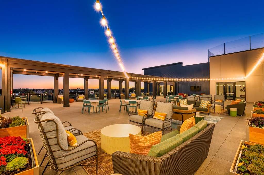 A rooftop patio with a long row of chairs and tables.