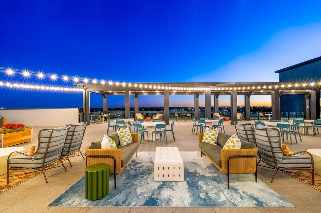 A rooftop patio with a long table and chairs under a string of lights.