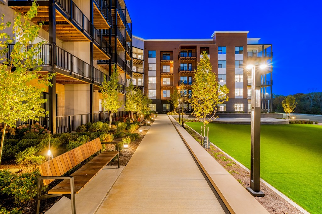 A long walkway with a bench and lights on either side leading to a building.