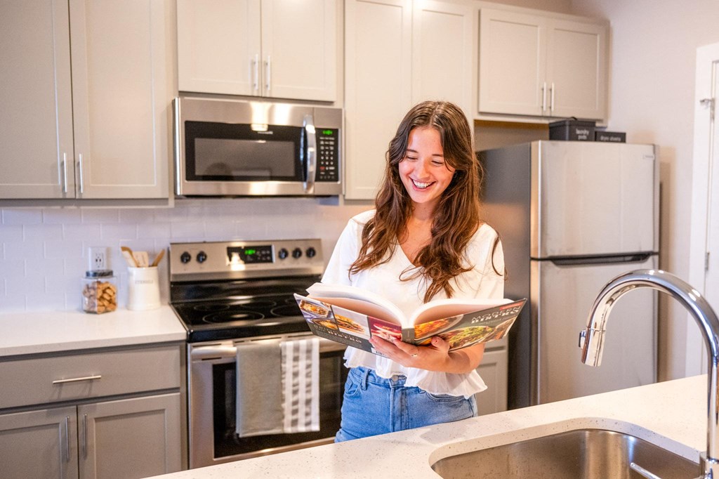 a woman standing in a kitchen reading a magazine