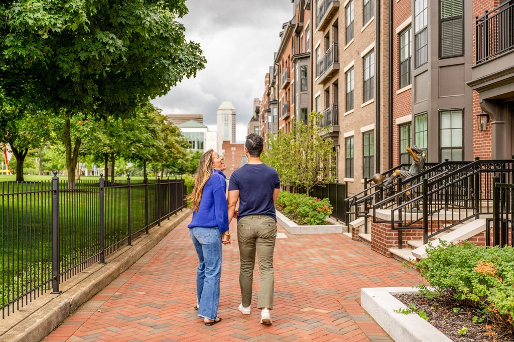 a couple walks down a brick sidewalk in front of an apartment building