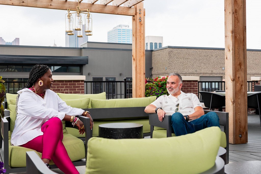 a man and a woman sit on a green couch on a rooftop patio
