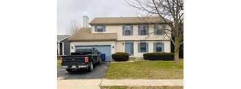 A black Ford truck is parked in front of a two-story house with a blue garage door.