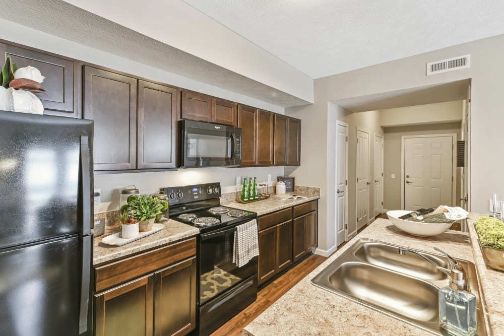 A kitchen with a black refrigerator and brown cabinets.