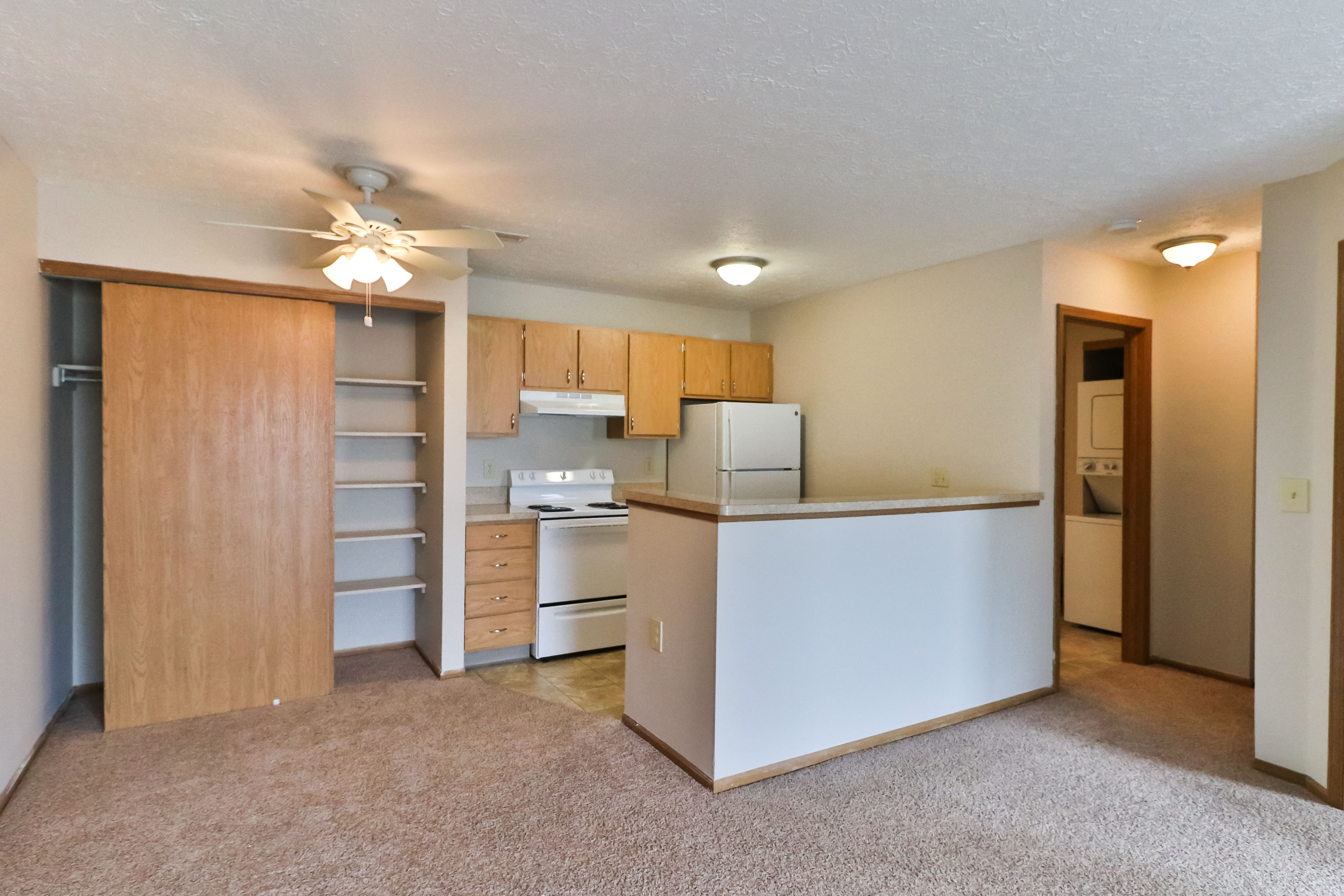 an empty living room with a kitchen and a ceiling fan