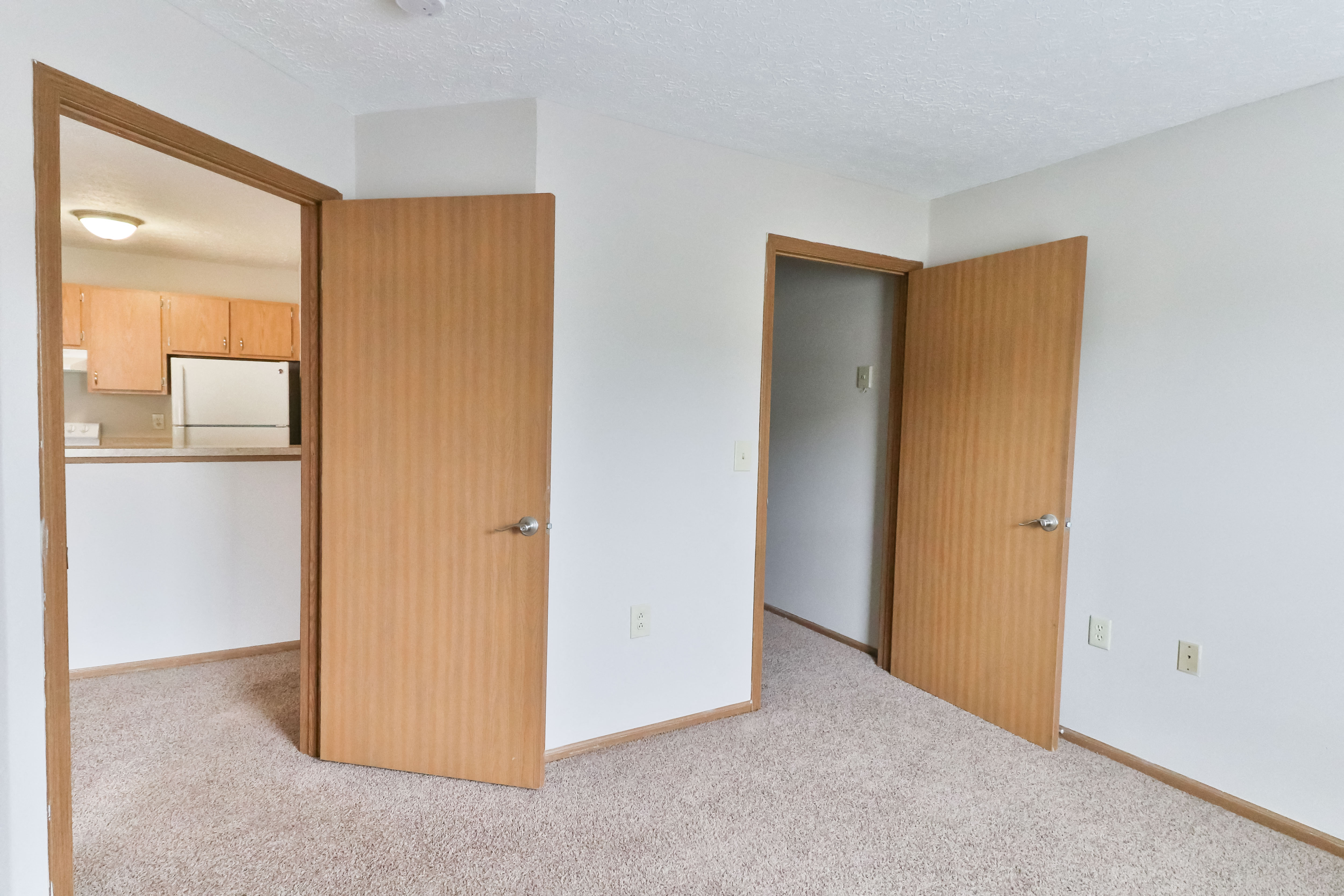 an empty bedroom with two doors and a kitchen