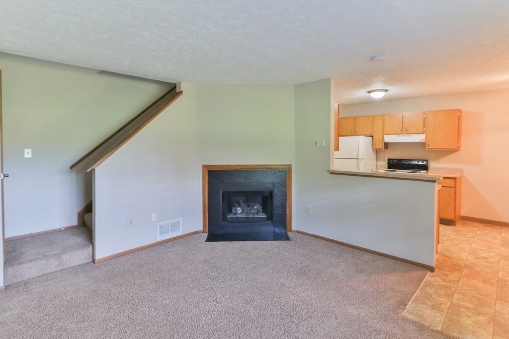 an empty living room with a fireplace and a kitchen
