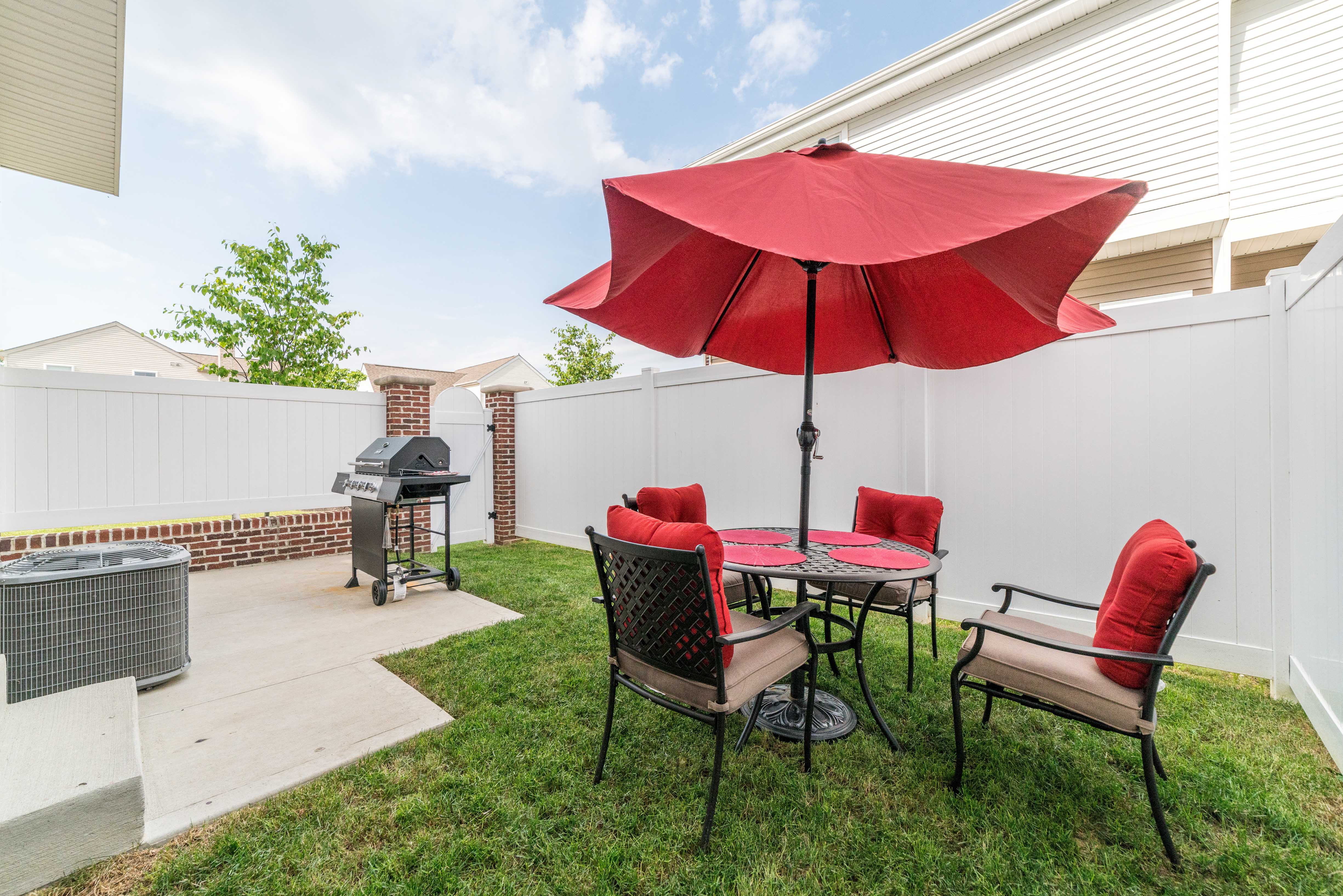 a patio with a table with a red umbrella and chairs and a grill