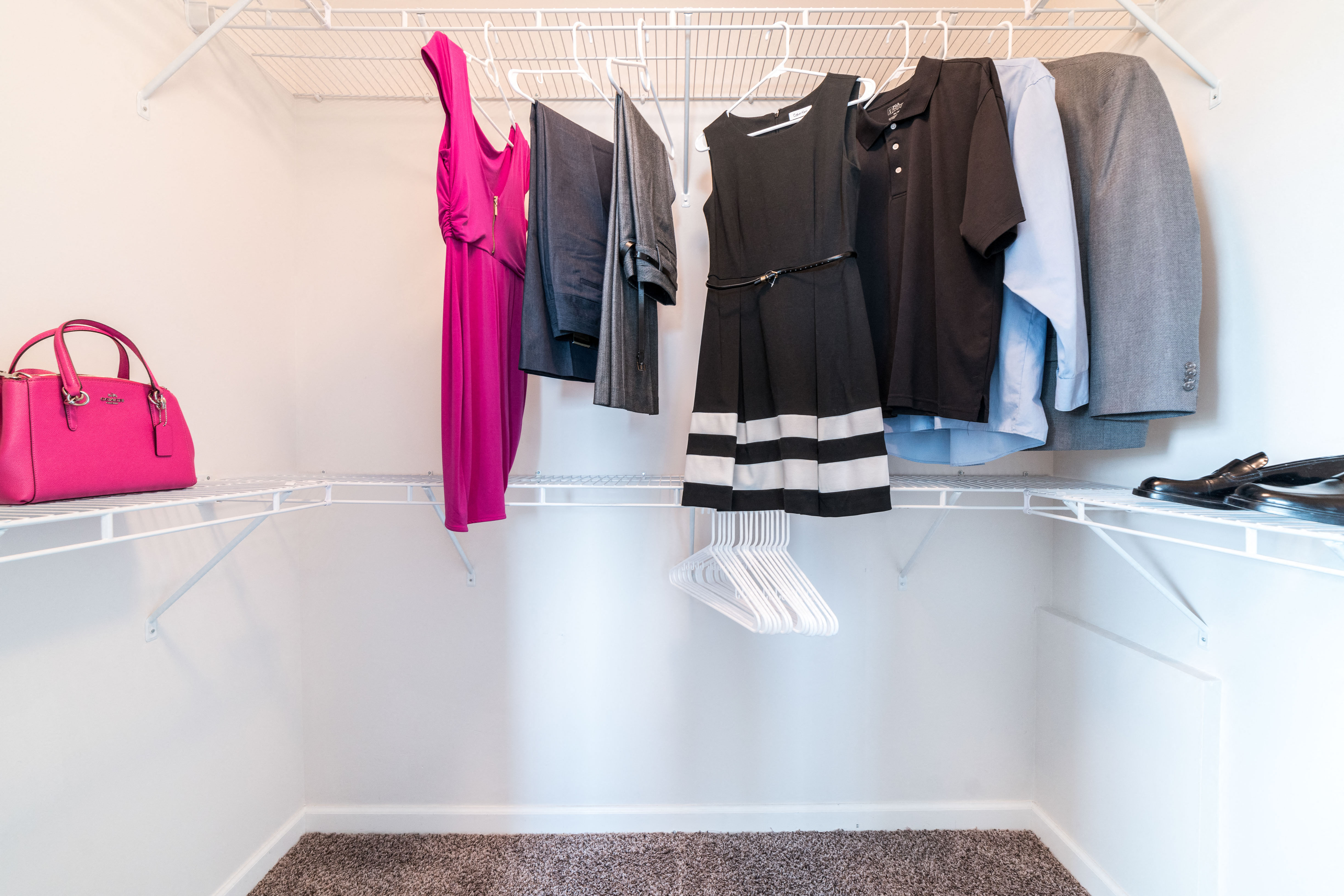 a closet with clothes hanging on a rack and a pink purse