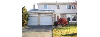 A house with a white garage door and a red bush.