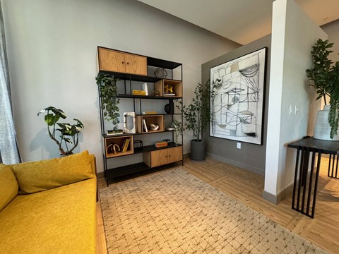 A living room with a yellow sofa and a black and white drawing on the wall.