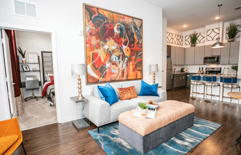 A living room with a large painting on the wall and a white couch with blue pillows.