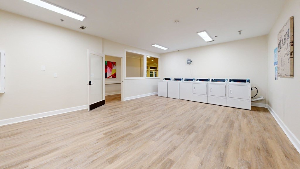 A room with wooden floors and white walls, with a row of white cabinets on the right side.