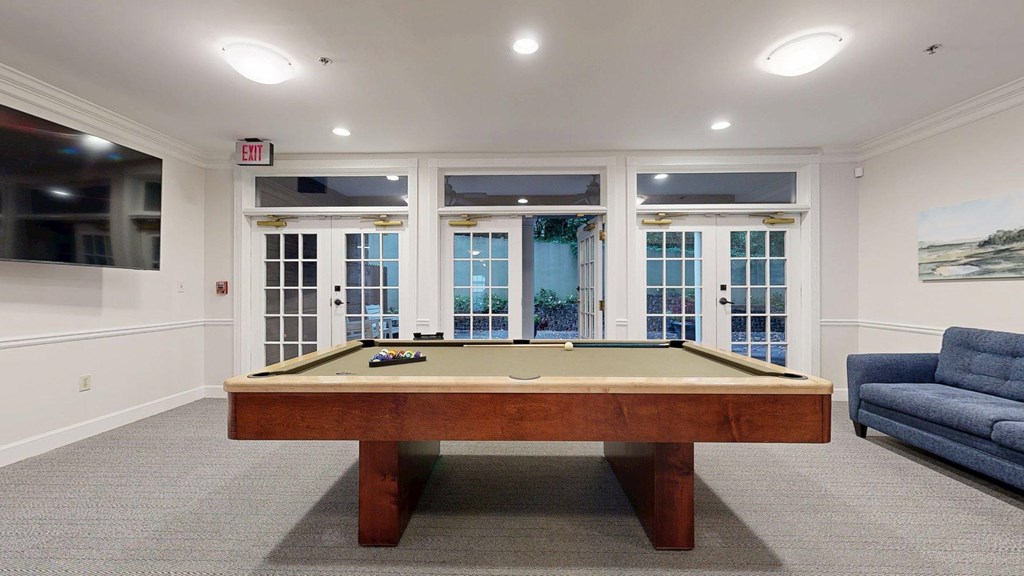 A pool table in a room with a couch and a window.