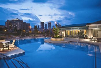 Nighttime view of community pool with Atlanta skyline in background at Ashley at Auburn Pointe in Atlanta, GA