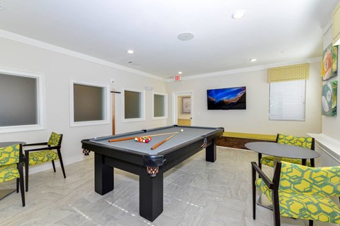 A room with a pool table and chairs.