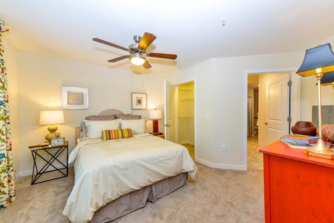 A bedroom with a bed, a ceiling fan, and a nightstand with a lamp.