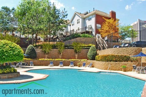 A pool surrounded by a wall and chairs with a building in the background.
