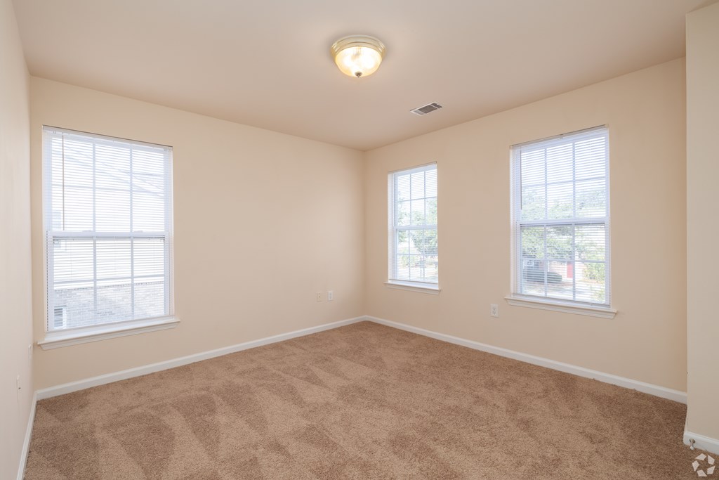 A room with beige carpet and two windows.