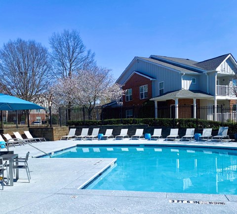 A swimming pool in front of a house with a fence and trees in the background.