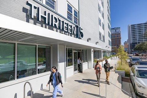 Three people are walking in front of a building with the number 13 on it.