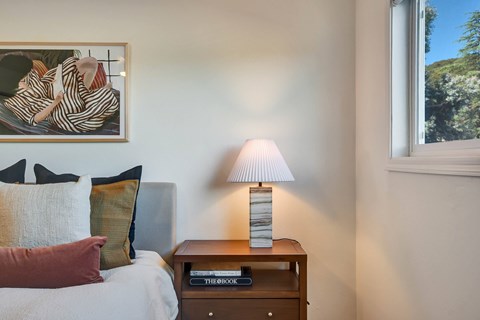 A bedroom with a bed, a nightstand with a lamp and a painting on the wall.