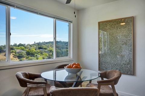 A dining room with a glass table and chairs and a view of the outdoors through the window.