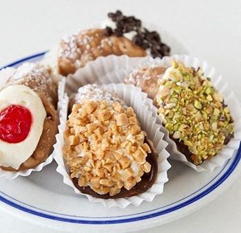 A plate of assorted pastries including a doughnut with a cherry on top, a chocolate-covered item with nuts, and a pastry with a white cream filling.