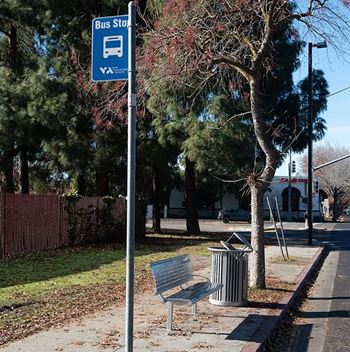 A bus stop sign is on a pole next to a bench.