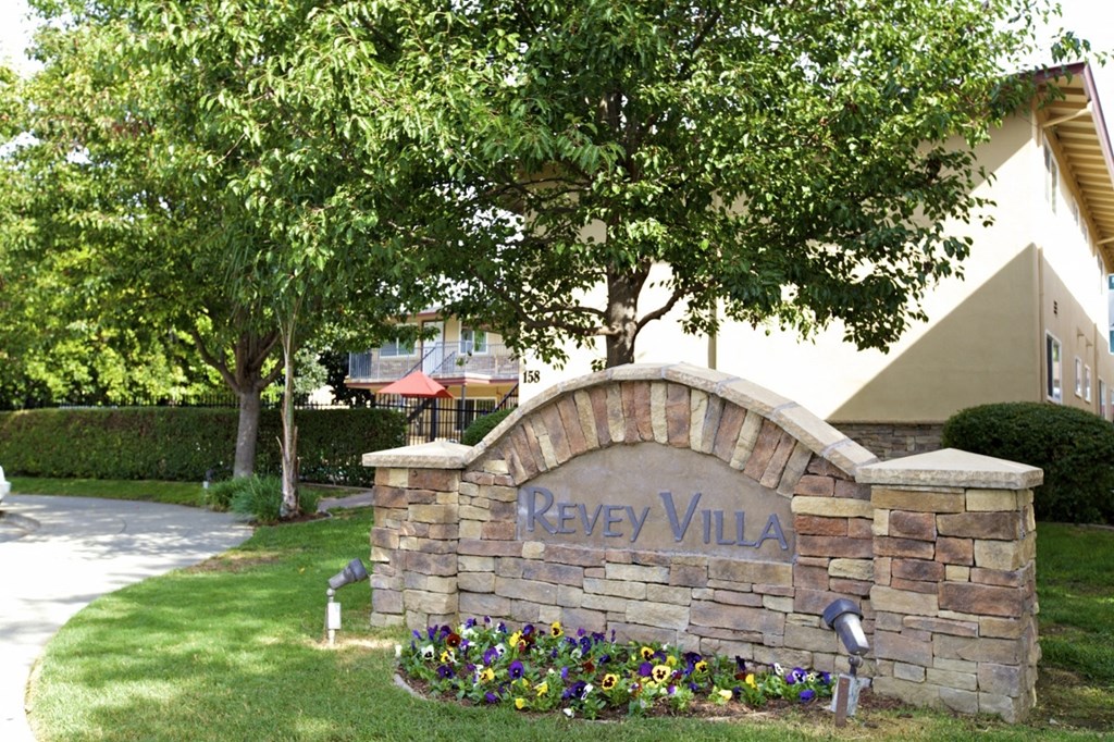 a stone sign that says in front of trees and flowers