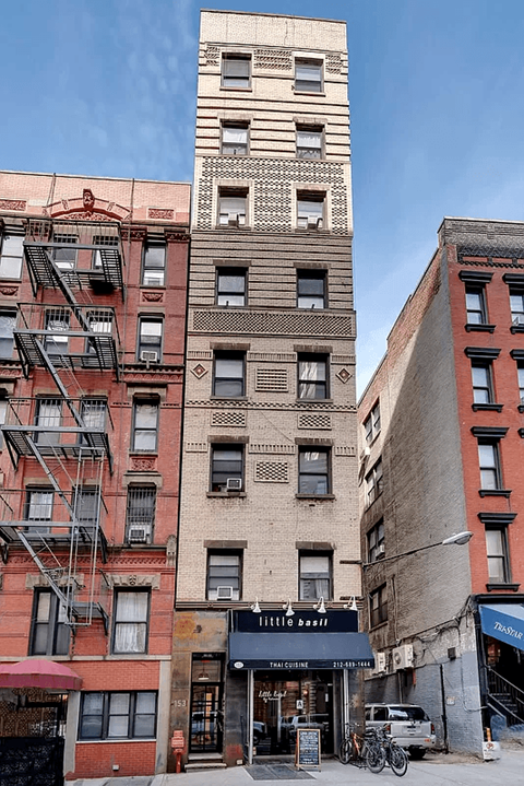 A tall building with a red awning is in front of a shorter building with a black awning.
