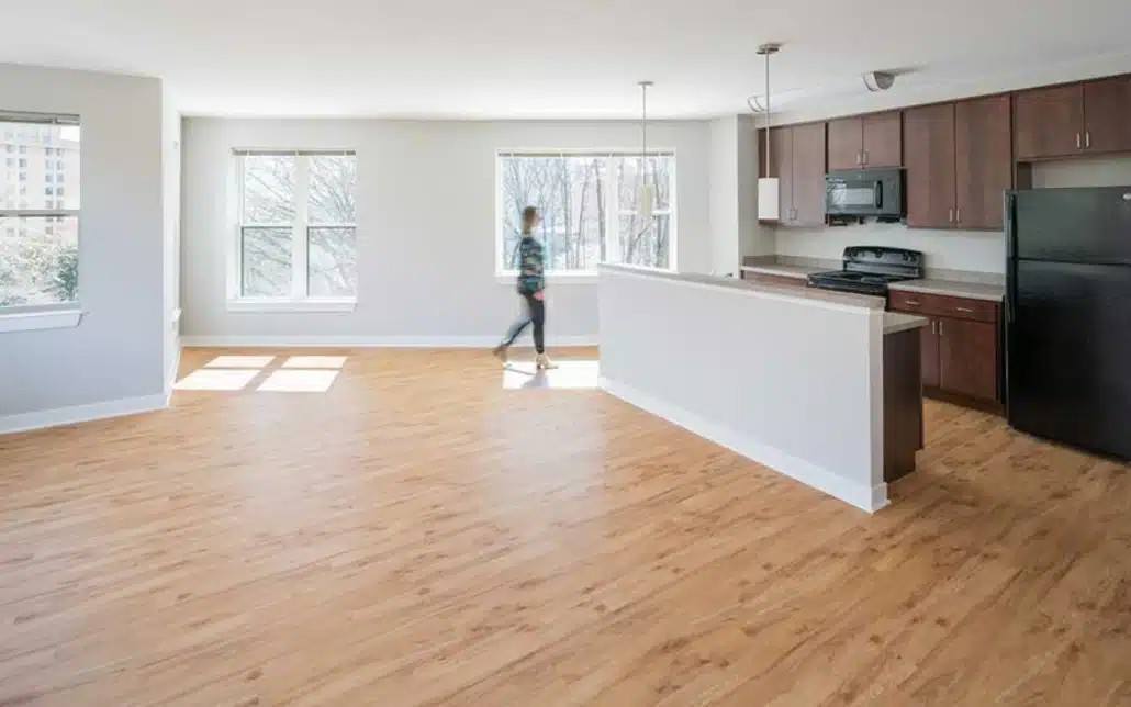 A person is walking in a spacious kitchen with wooden floors and white walls.