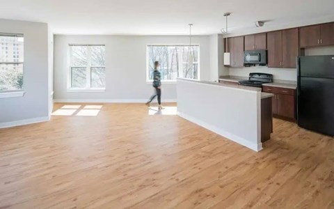 A person is walking in a spacious kitchen with wooden floors and white walls.