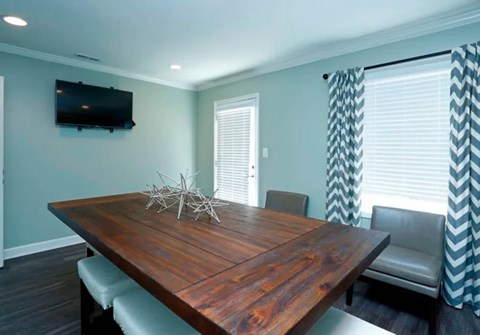 A wooden dining table with chairs and a TV mounted on the wall.