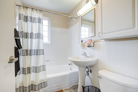 A bathroom with a white sink, a white tub, and a window with a curtain.