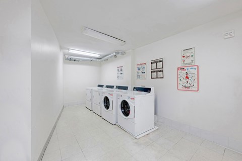 A laundry room with three washing machines and a white wall.