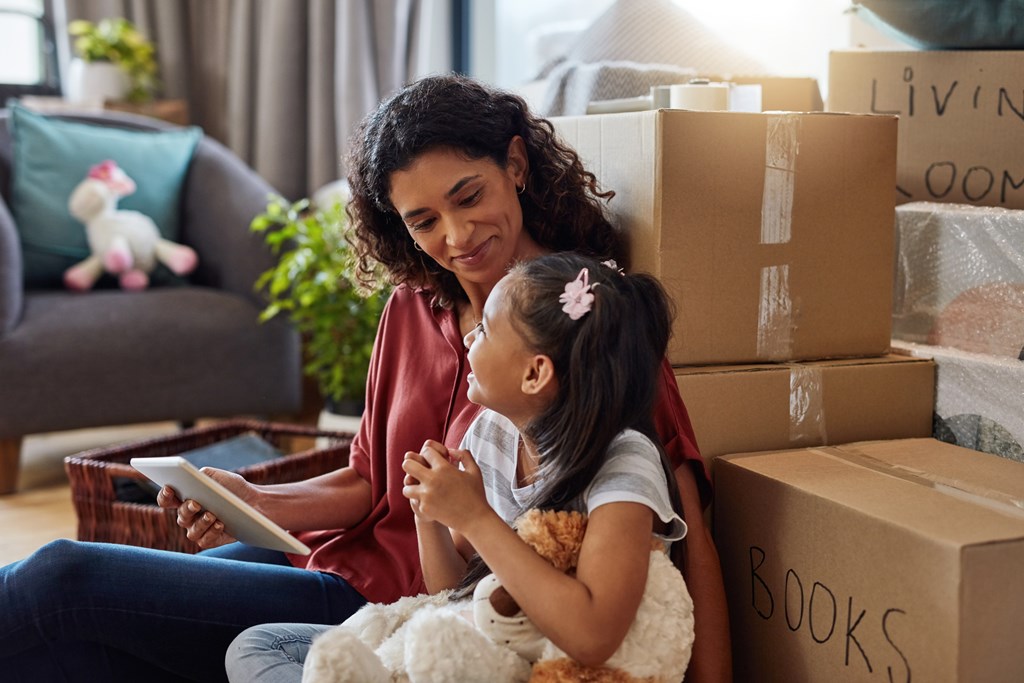 A woman and a young girl are surrounded by moving boxes in a living room.