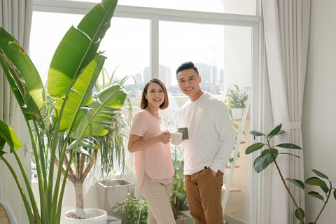 A man and woman standing in a room with a large window and plants.