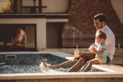 A man and a child are sitting by a pool.